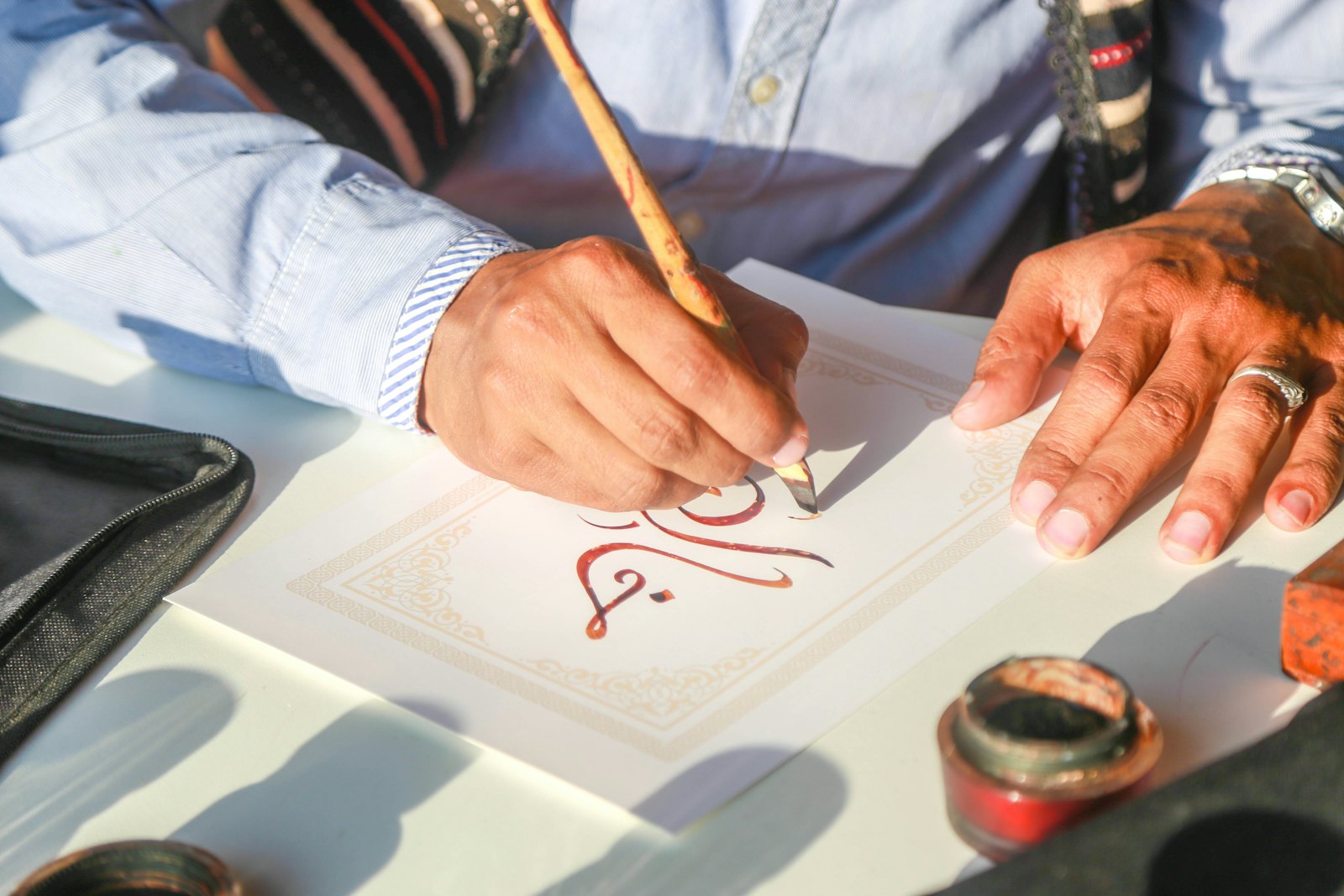 An adult's hands writing Arabic calligraphy with a reed pen